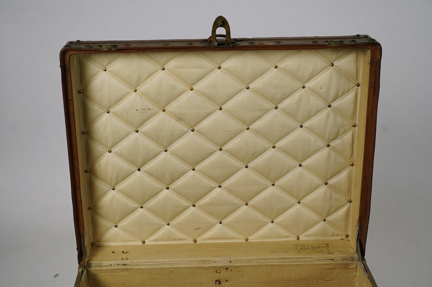 A vintage Louis Vuitton trunk, with brass and leather mounts and studded wooden slats, in plain beige canvas, with label for Paris and London, number 159008, 61cm wide, 48cm deep, 53cm high